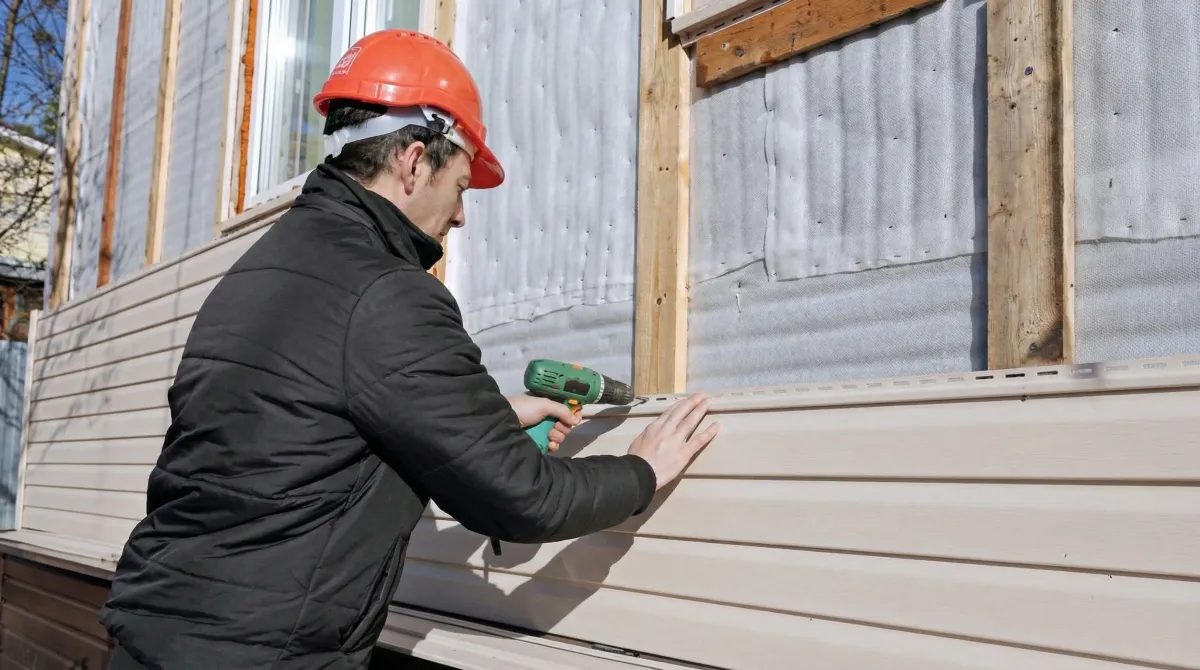 Siding replacement professional using a power drill to install new tan vinyl siding on a home exterior in Raleigh, NC